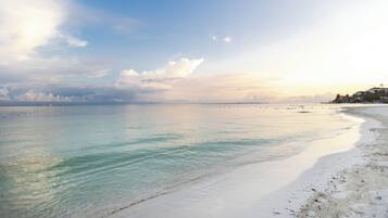 A beach with clear water, a sandy shore, and a distant shoreline with buildings.
