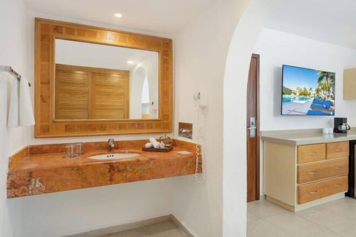 A bathroom with a wooden vanity, a large mirror, a sink, and a television mounted on the wall.