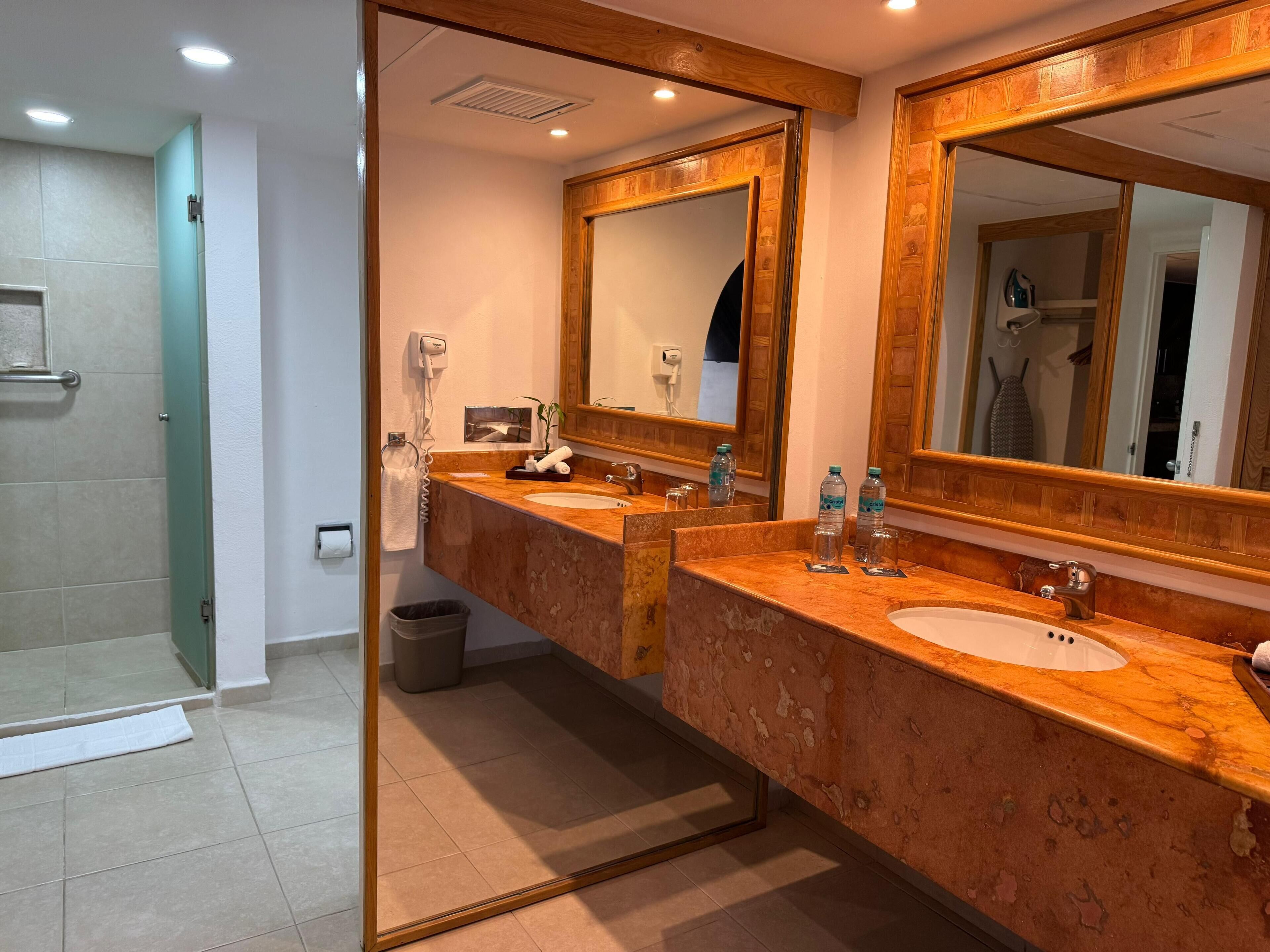 Une salle de bain d’hôtel avec deux lavabos, de grands miroirs, un porte-serviettes et un sèche-cheveux.