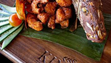 A wooden serving board with fried fish and vegetables, branded with "KINHA RESTAURANT".