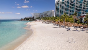 A beach with white sand, clear turquoise water, and a row of hotel buildings with balconies overlooking the beach.