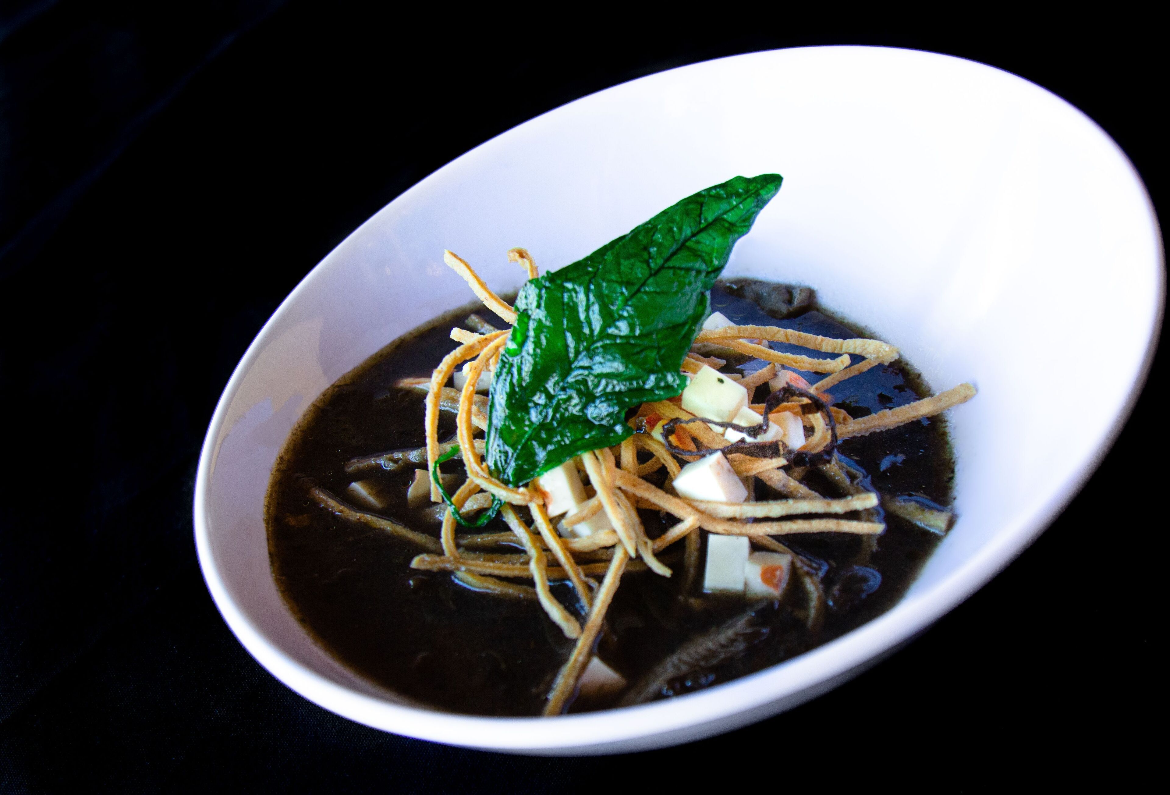 A bowl of soup with noodles, tofu, and a green leaf garnish.