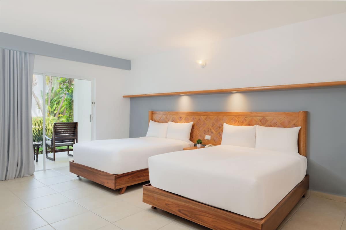 A hotel room with two wooden beds, a sliding glass door leading to a balcony, and a small potted plant on the nightstand.