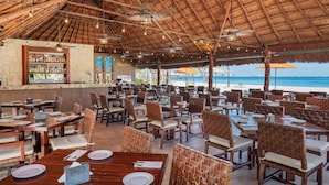 A beachside restaurant with wooden tables and chairs, a bar area, and a view of the ocean. - Beachscape Kin ha Villas & Suites (Cancun)