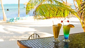 A table with two drinks, a beach view, and palm trees. - Captain Morgan's Retreat (San Pedro)
