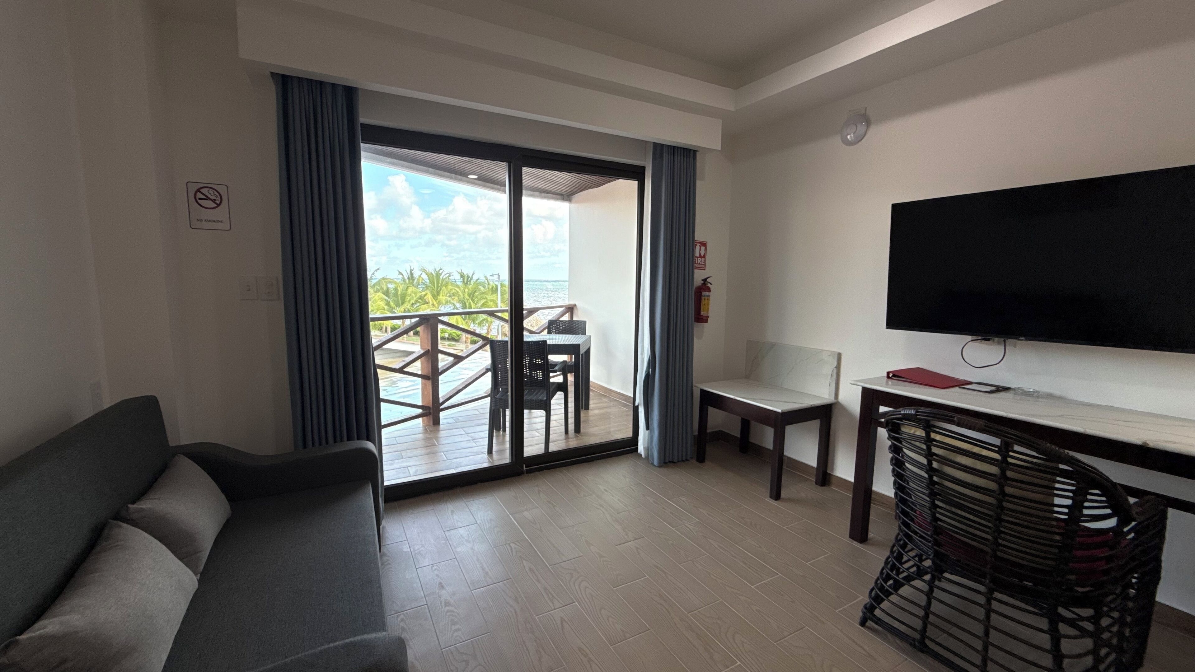 A hotel room with a sofa, a TV, a desk, and a view of the sea through a sliding door.