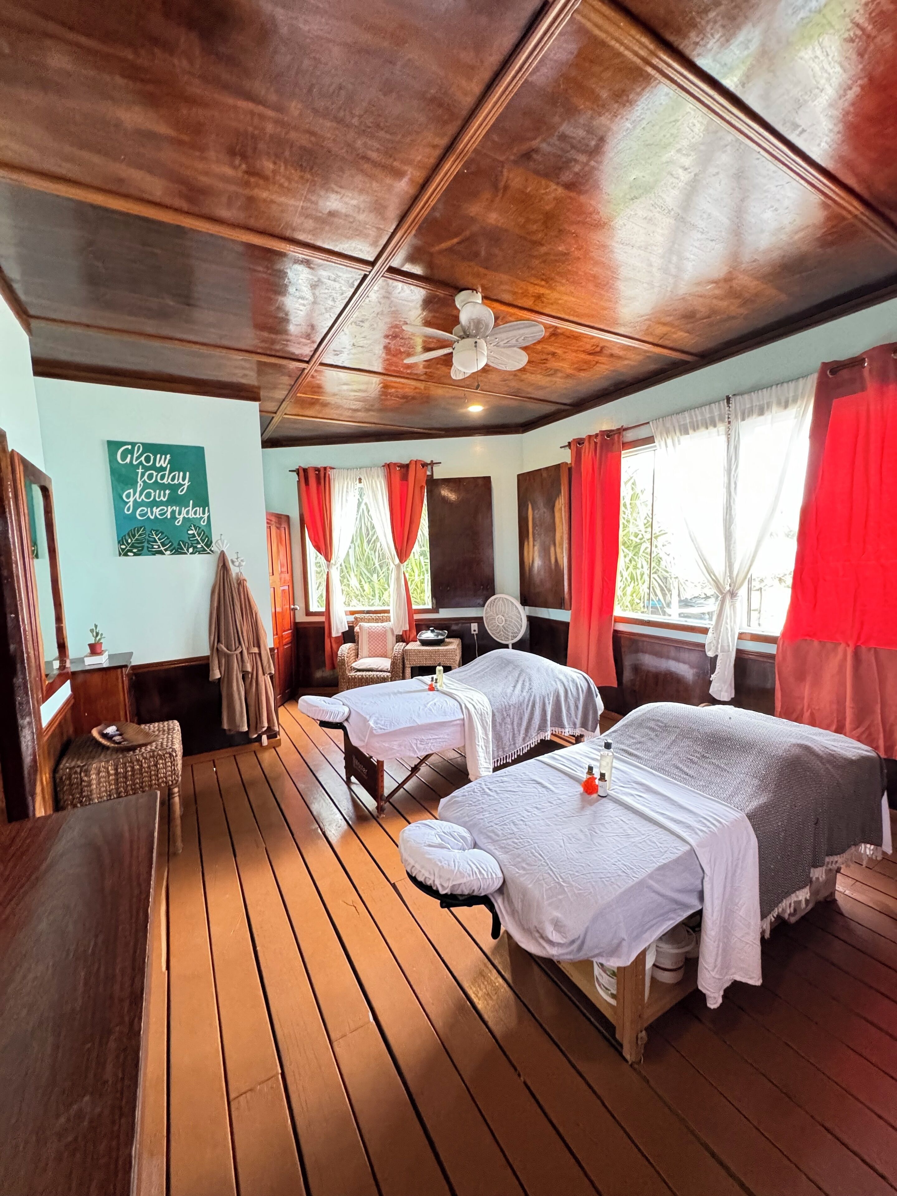 Ein Zimmer mit Holzboden, zwei Betten, einem Deckenventilator und einem Wandzeichen.