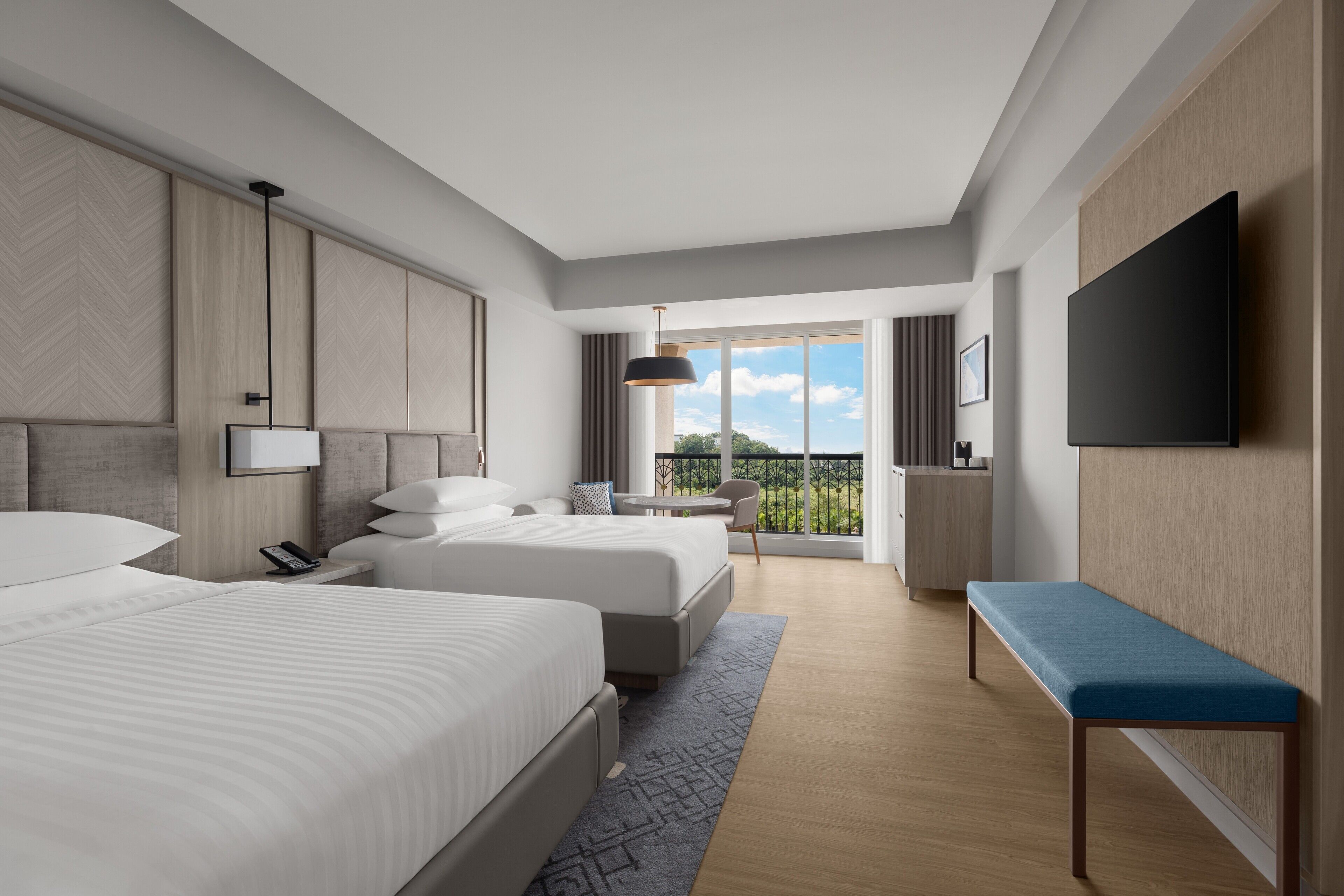 Una habitación de hotel moderna con dos camas, televisión, balcón con vistas y escritorio con silla.