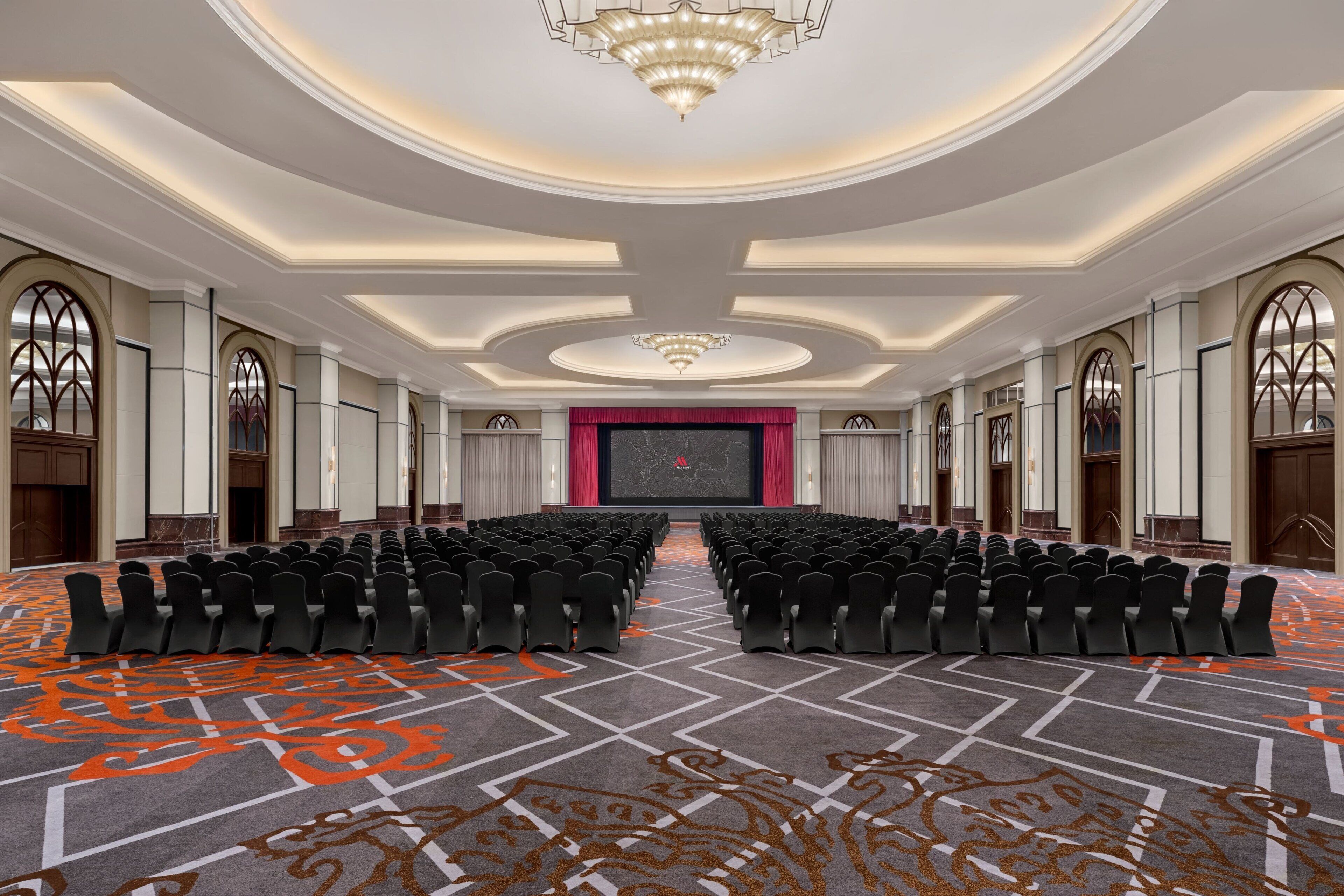 A conference room with rows of chairs, a large screen, and a chandelier.
