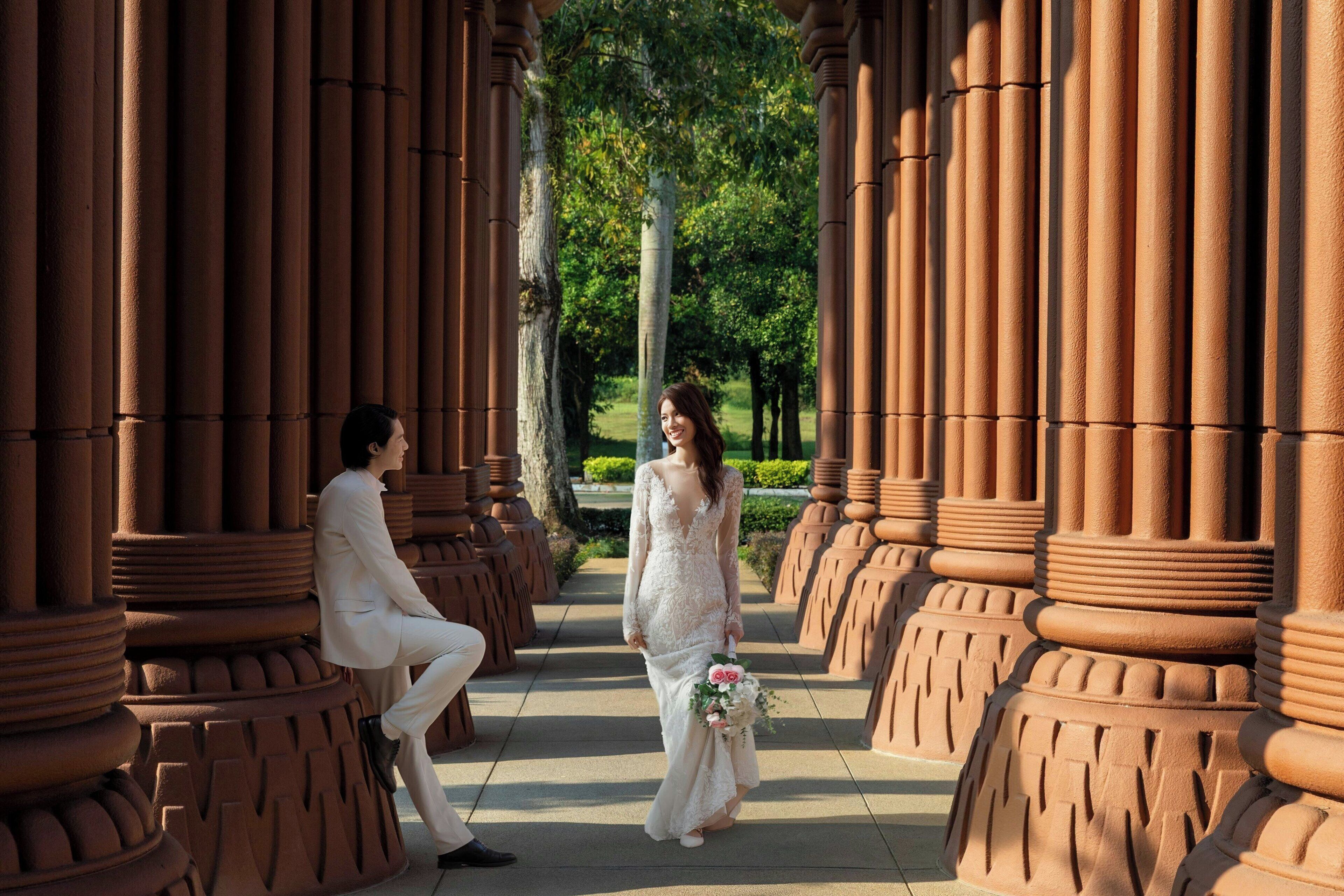 A wedding ceremony in a covered outdoor area with columns and greenery.