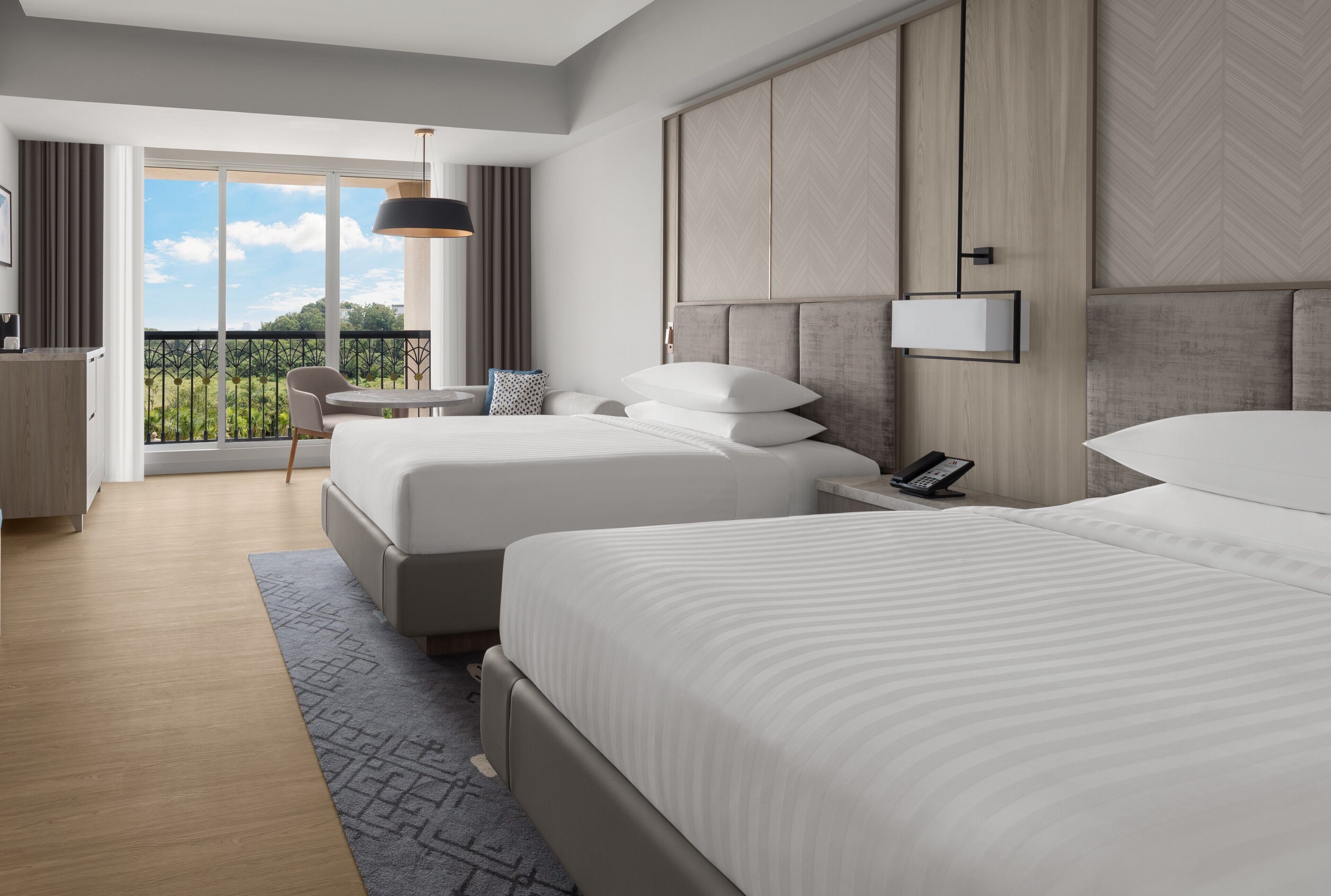 Una habitación de hotel moderna con dos camas, un balcón con vistas y un escritorio con silla.