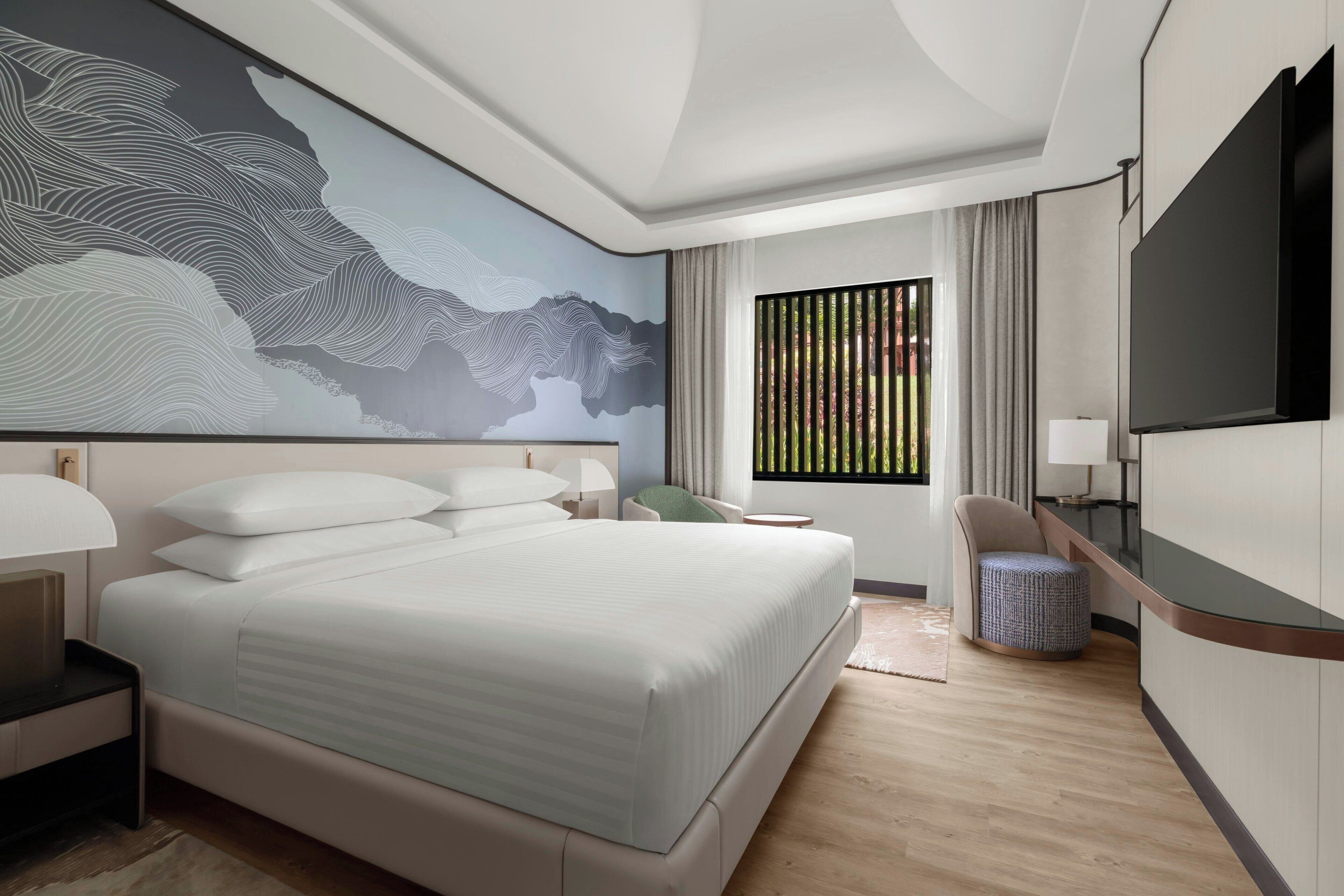 A modern hotel room with a large bed, a flat-screen TV, a desk with a chair, and a large abstract mural on the wall.