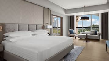 A modern hotel room with a large bed, a sofa, a chair, and a balcony with a city view.
