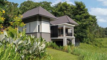 A modern two-story house with a balcony, surrounded by lush greenery and a well-maintained lawn.