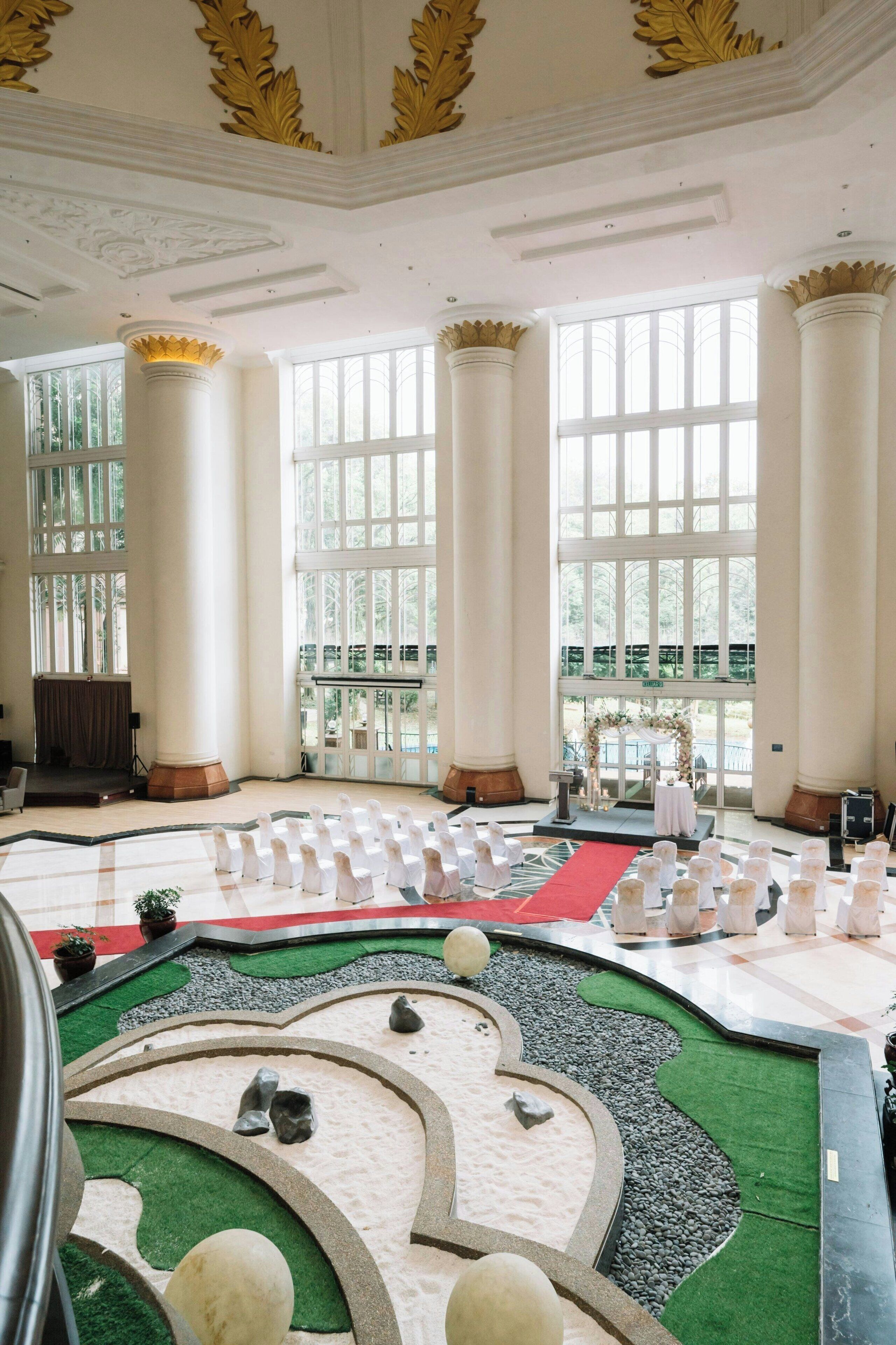A spacious hall with large windows, a stage, and rows of white chairs.