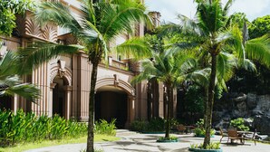 Un patio con palmeras, mobiliario exterior y un edificio de arquitectura clásica.