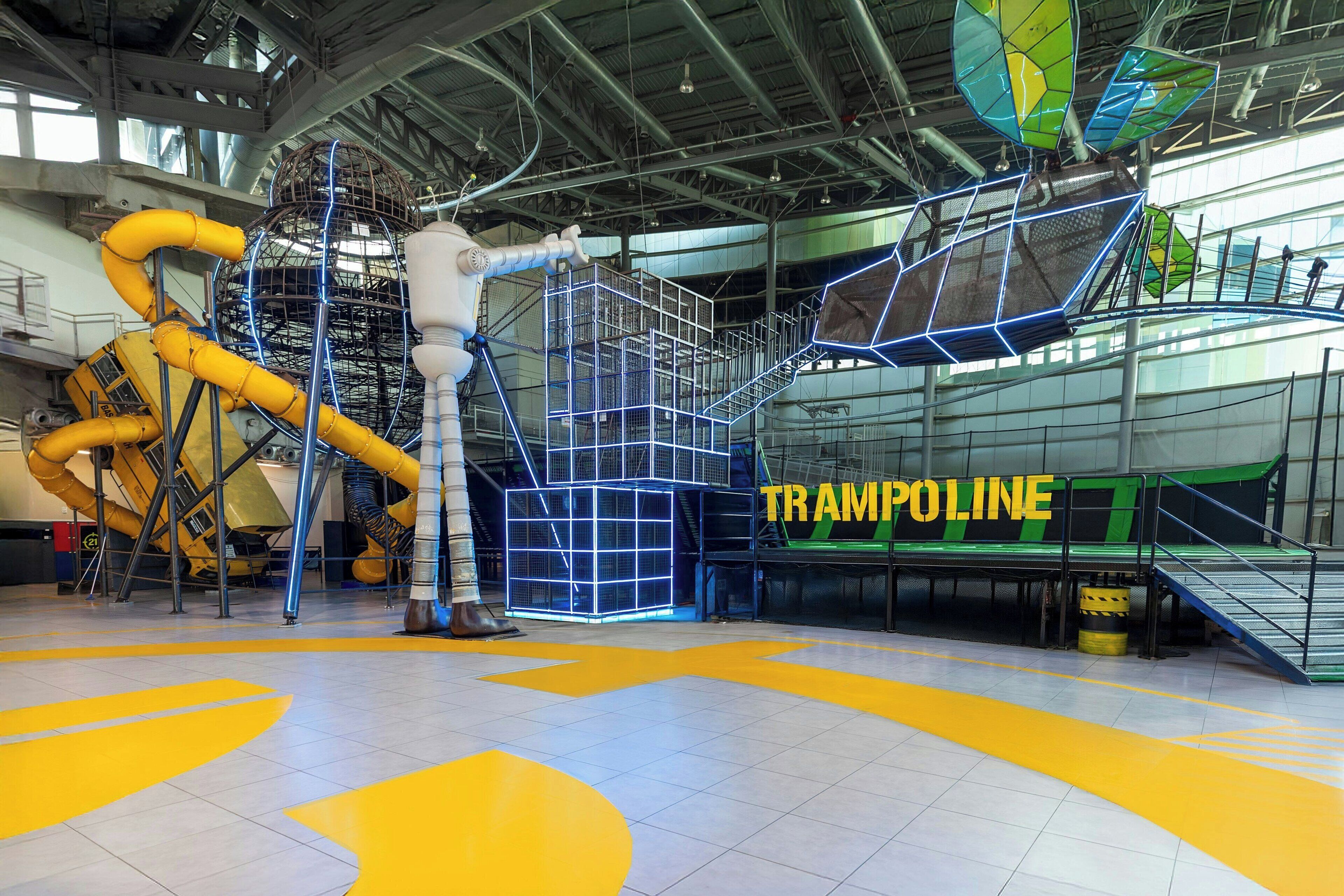 An indoor amusement area with a large trampoline and various play structures.