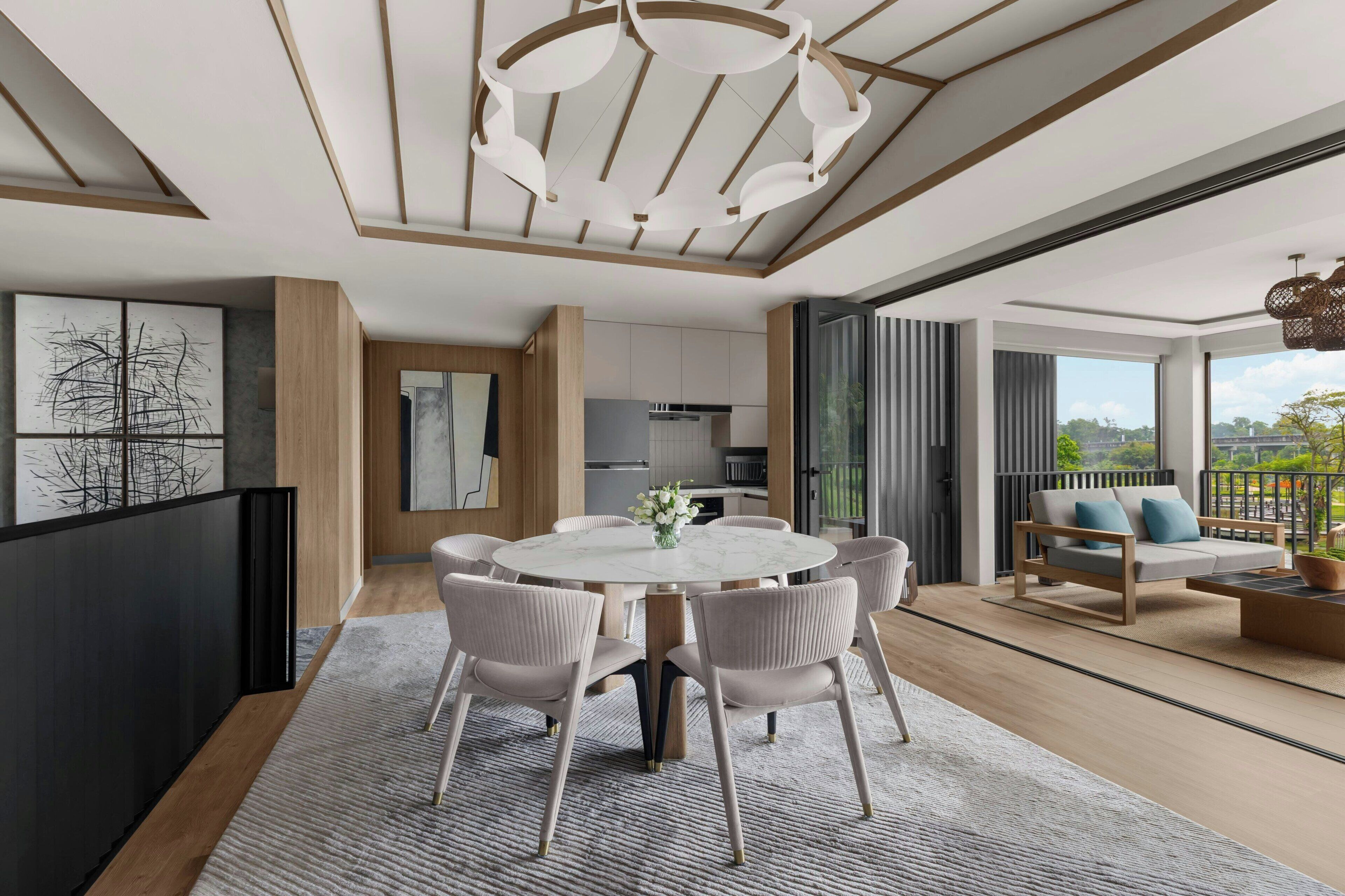 A modern dining area with a round table and chairs, a kitchen in the background, and a balcony with a sofa.