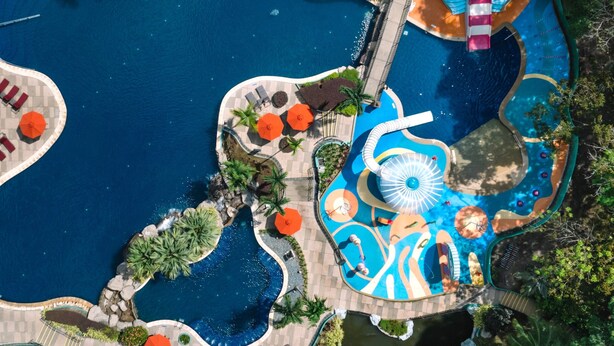 Vista aérea de un resort con varias piscinas, palmeras y un tobogán de agua.