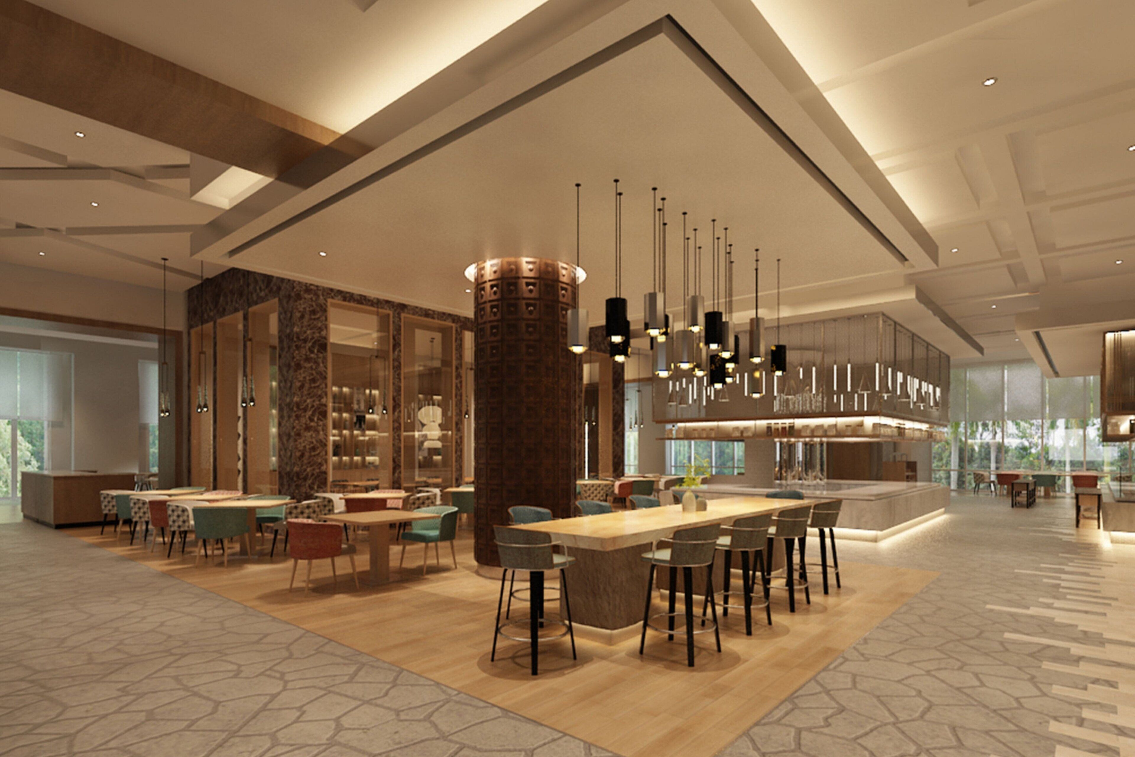 A spacious, modern hotel lobby with a central bar area, seating arrangements, and a large window providing natural light.