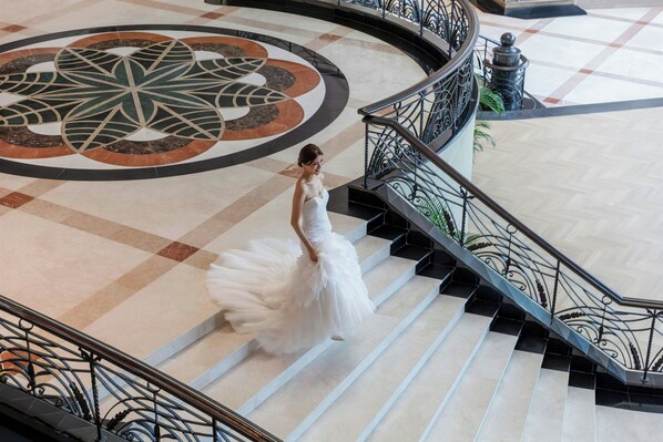 A woman in a white dress descending a grand staircase with ornate railings and a decorative floor pattern. - Putrajaya Marriott Hotel (Serdang)