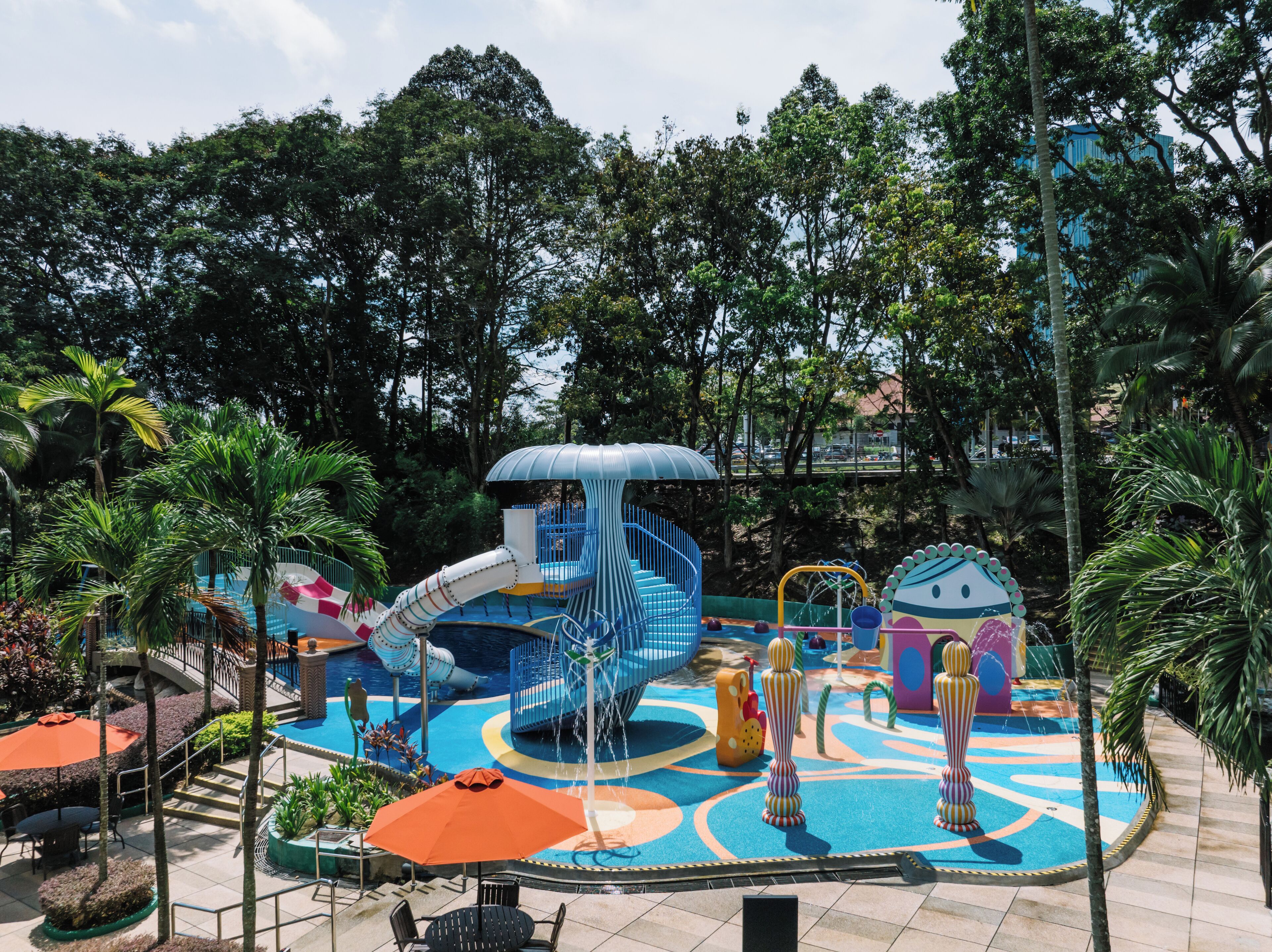 Parque acuático con tobogán, estructuras de juego y zona de piscina rodeada de palmeras y follaje.