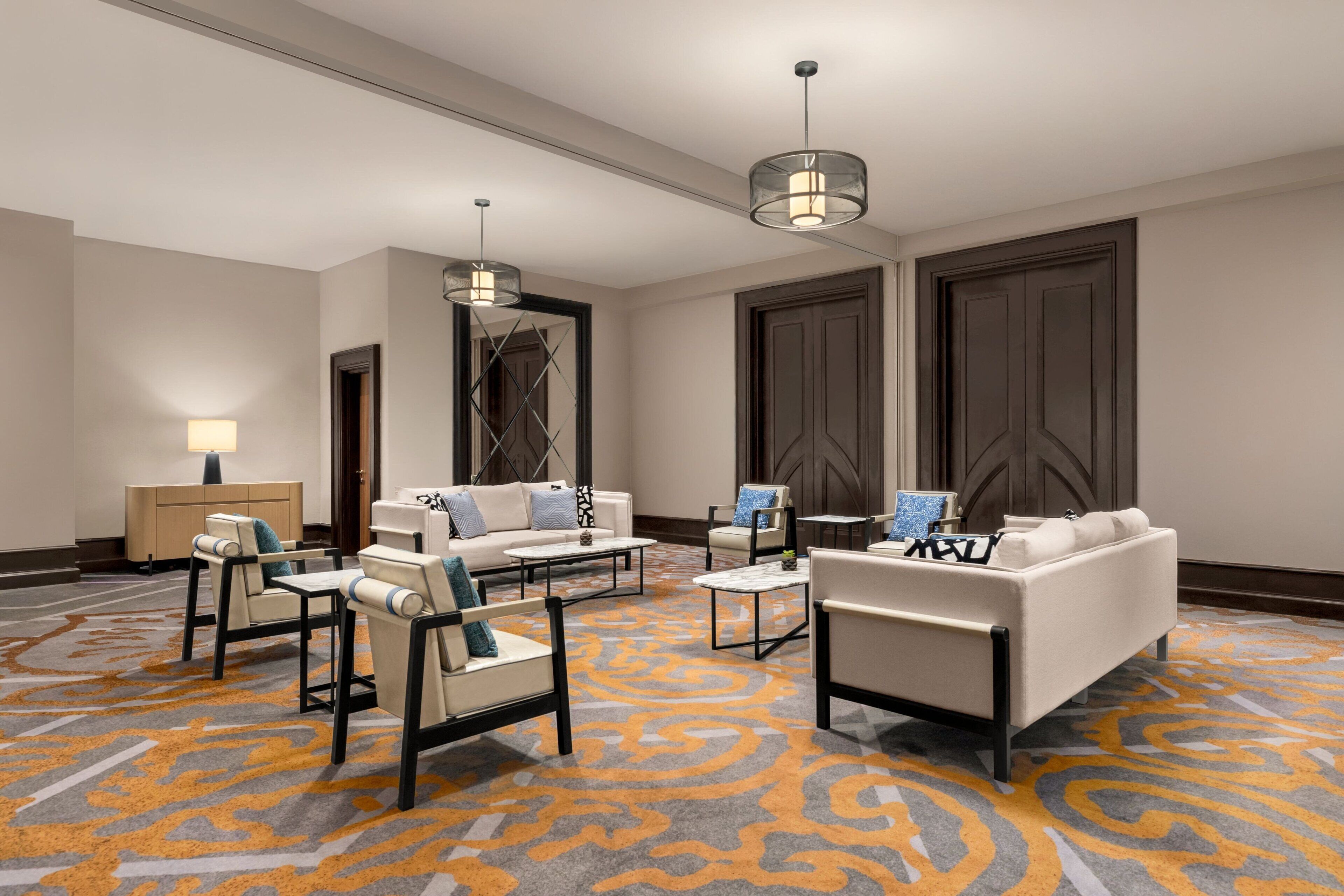 Een hotel lobby met een modern ontwerp, met een zithoek met banken en fauteuils, een salontafel en een kamerbreed tapijt.