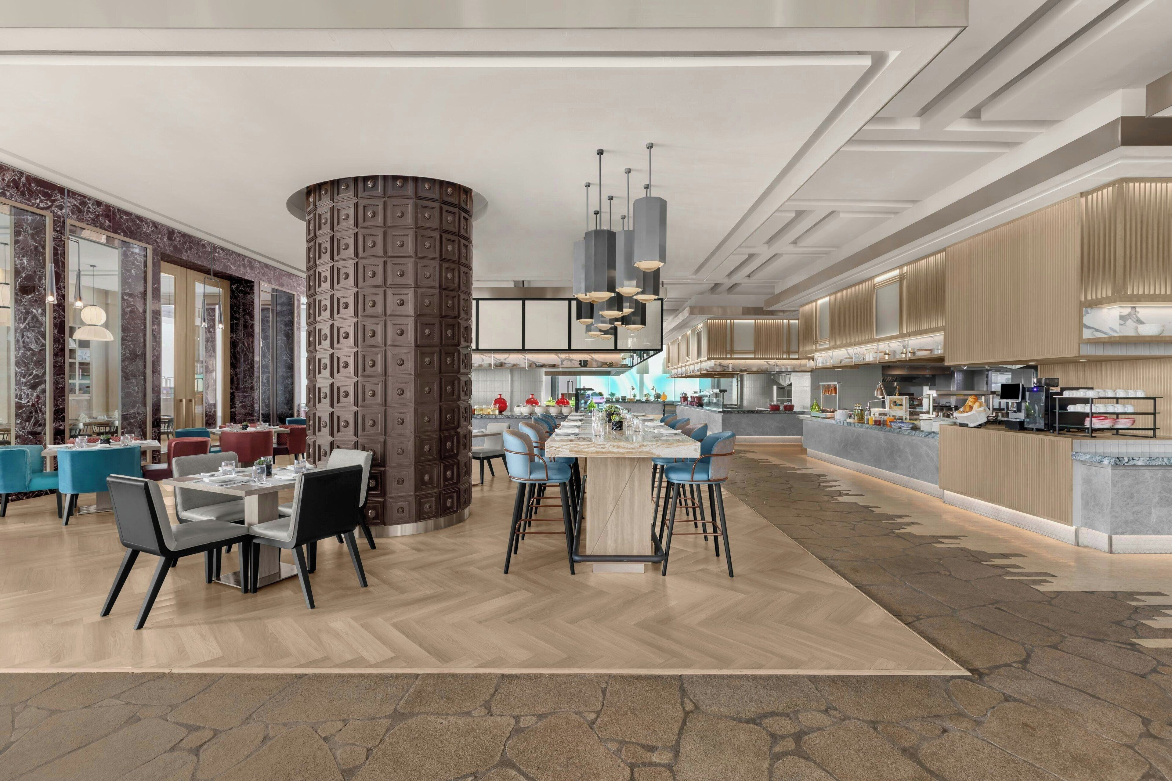Un hall d’hôtel spacieux avec un bar central, de nombreux espaces de détente et une cuisine moderne visible au fond.