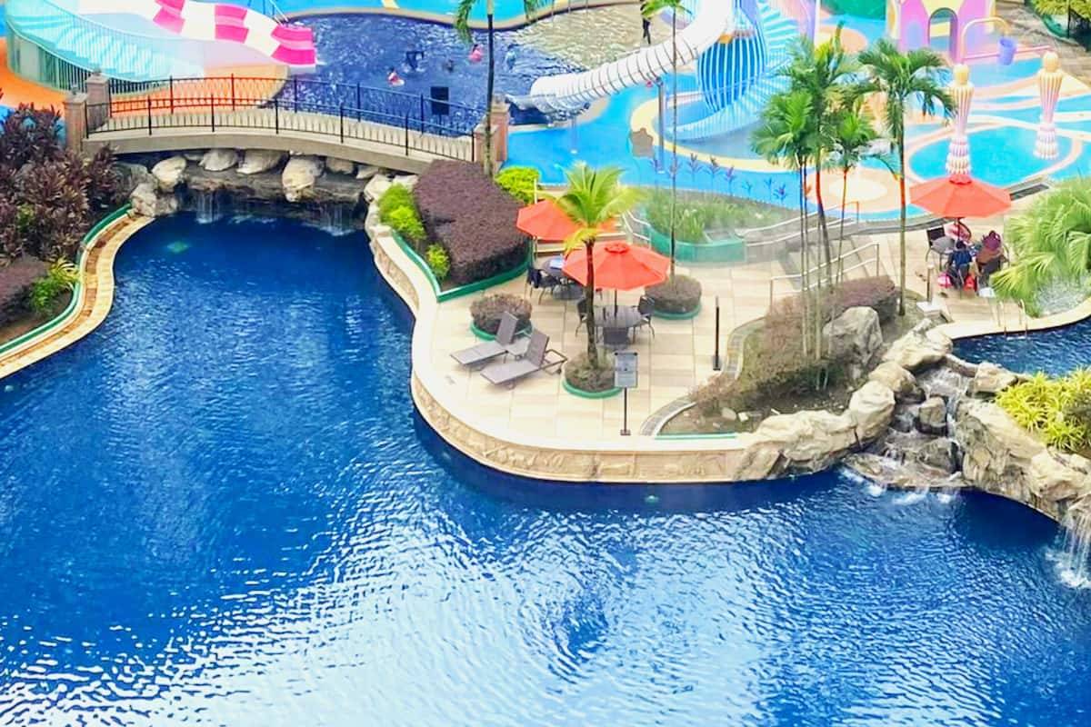 Una gran piscina con un puente, palmeras y un tobogán de agua.