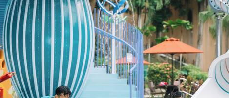 Un parque acuático con un tobogán en espiral azul y blanco, un flotador con forma de pato y un tobogán de agua.