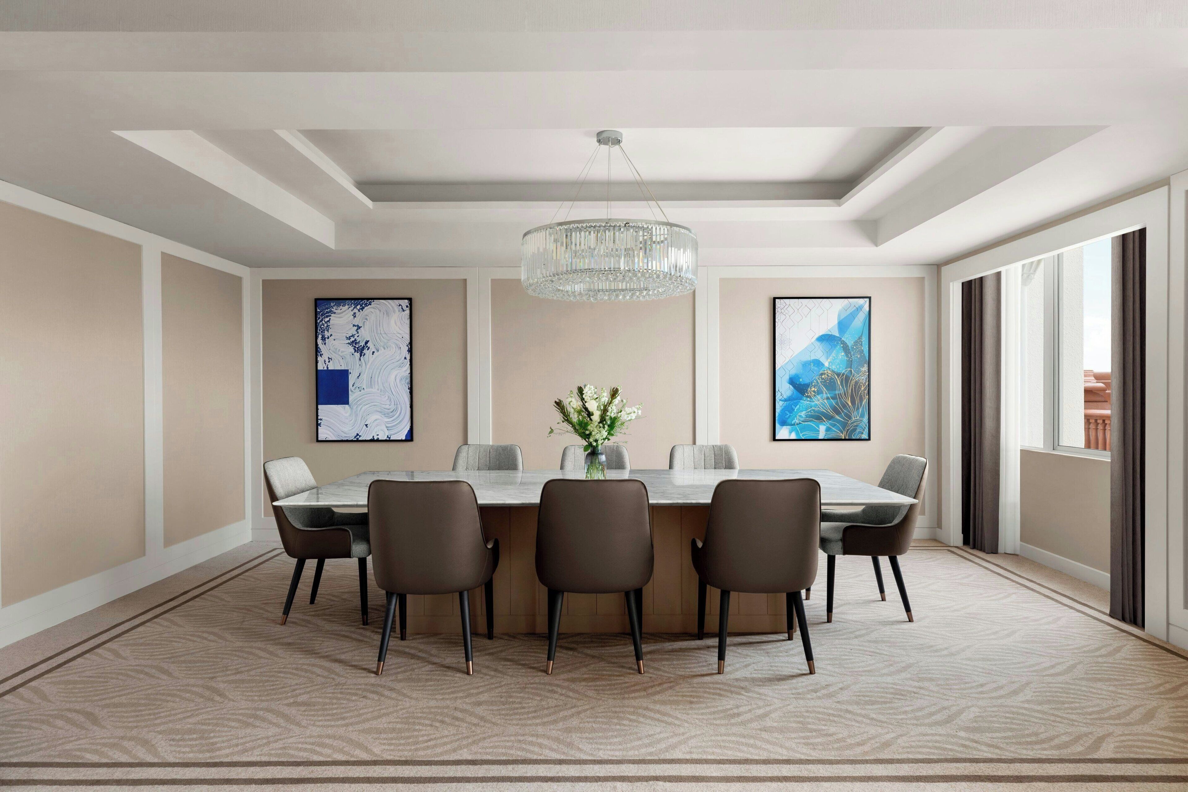 A modern dining room with a rectangular table, six chairs, a chandelier, and abstract art on the walls.