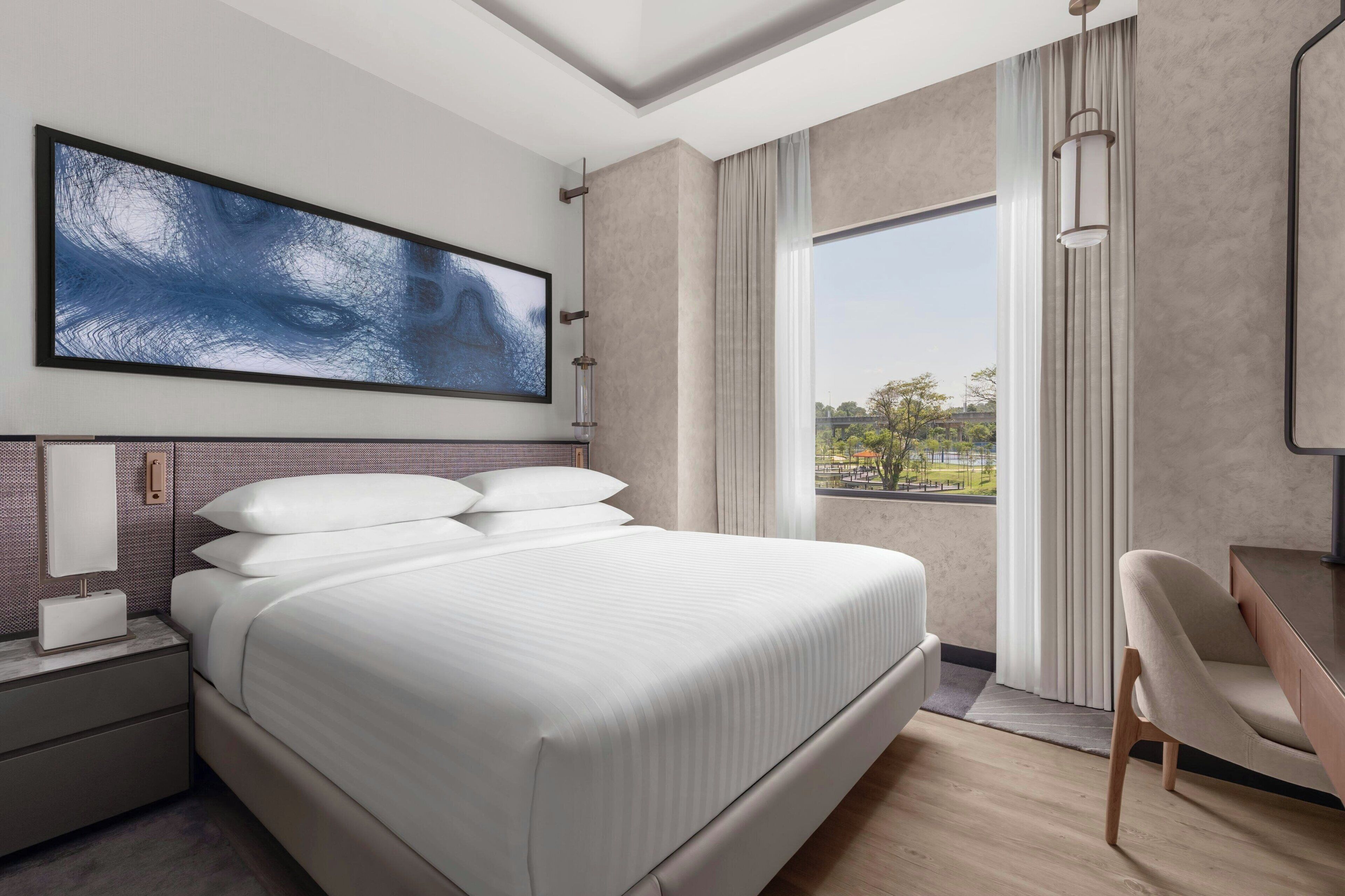 A modern hotel room with a large bed, a desk, and a view of the outdoors.
