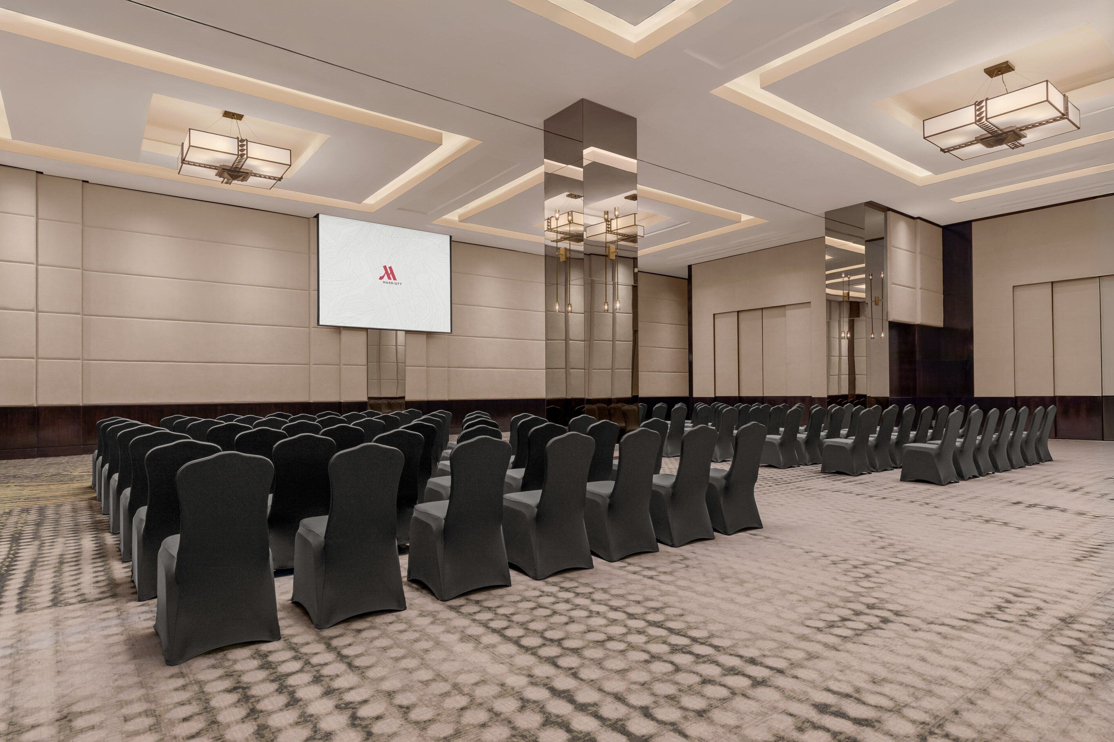 A conference room with rows of chairs, a projector screen, and modern lighting fixtures.