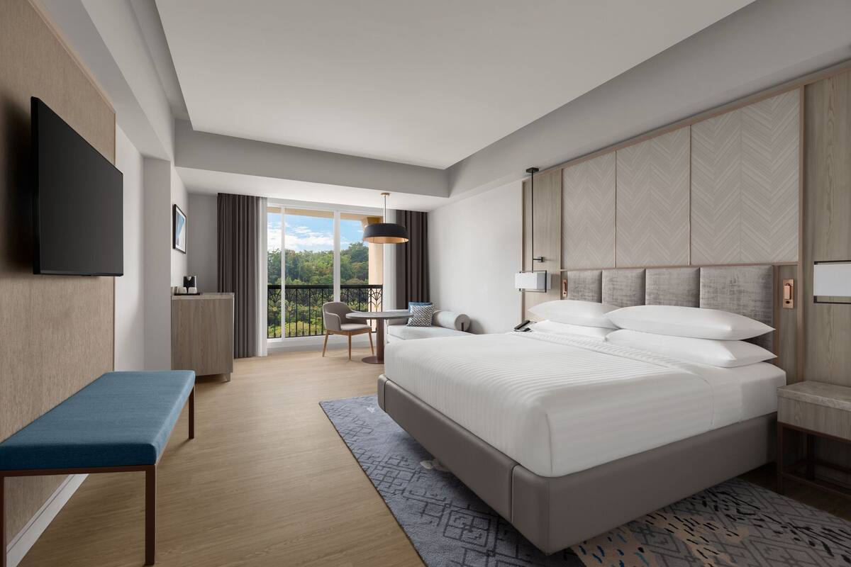 Una habitación de hotel moderna con una cama grande, un escritorio y un balcón con vistas.