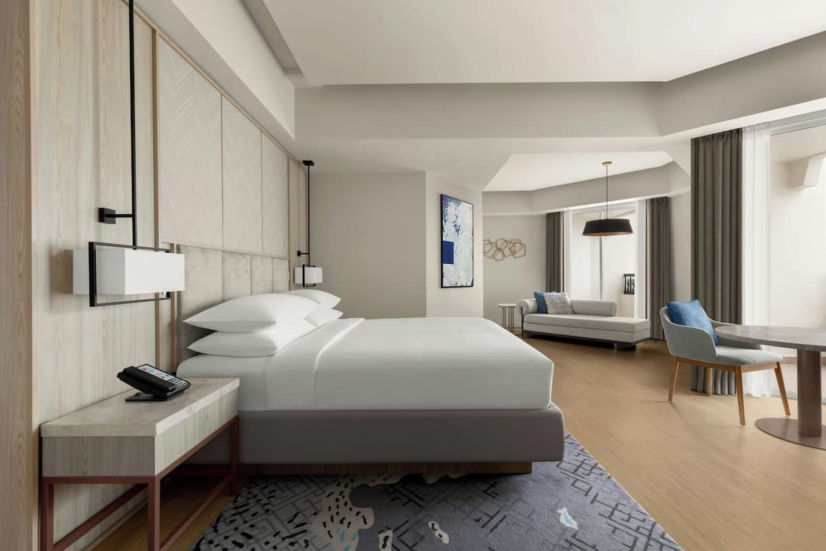 Una habitación de hotel moderna con una cama grande, un escritorio con teléfono, un sofá y una mesa de comedor.