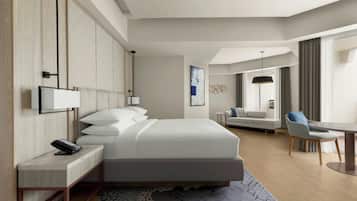A modern hotel room with a large bed, a desk with a phone, a sofa, and a dining table.