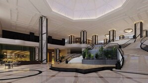 Un hall espacioso con techo alto, una escalera central y un área de descanso con mesas y sillas.