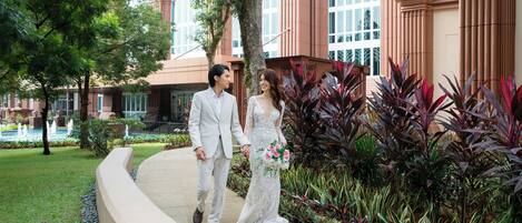 A couple walking on a pathway surrounded by lush greenery and a building with large windows and columns.