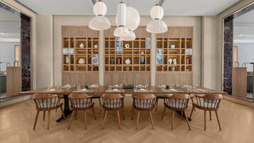 Een moderne eethoek met een lange houten tafel en stoelen, hanglampen en een decoratieve wand met planken.