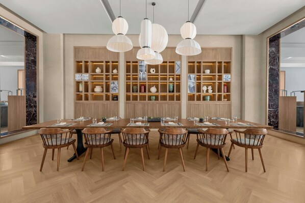 A modern dining area with a long wooden table and chairs, pendant lighting, and a decorative wall with shelves. - Putrajaya Marriott Hotel (Serdang)