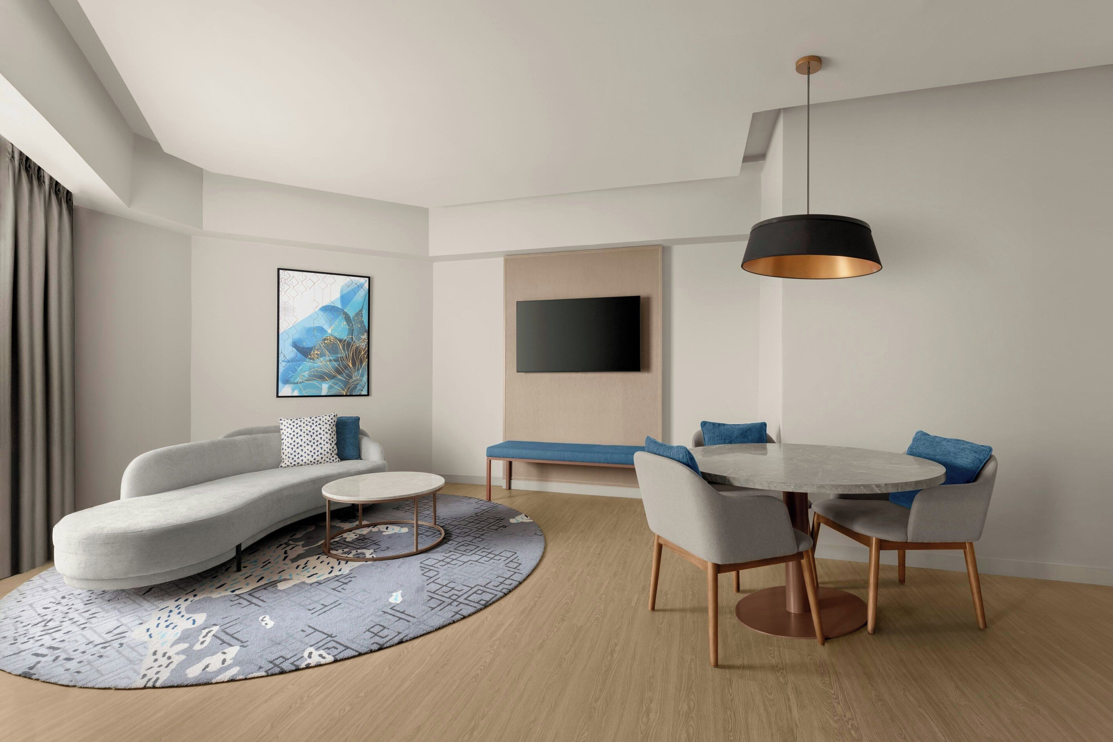 Una sala de estar moderna con un sofá, una mesa de centro, una mesa de comedor y sillas. Hay un televisor de pantalla plana montado en la pared y una lámpara colgante sobre la mesa de comedor.