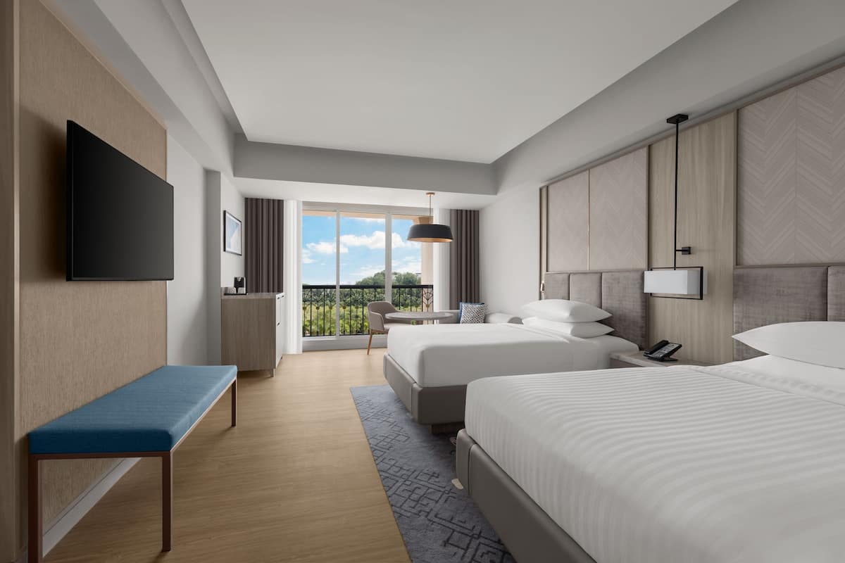 Una habitación de hotel moderna con una cama grande, una cama más pequeña, un banco, un escritorio y un televisor.