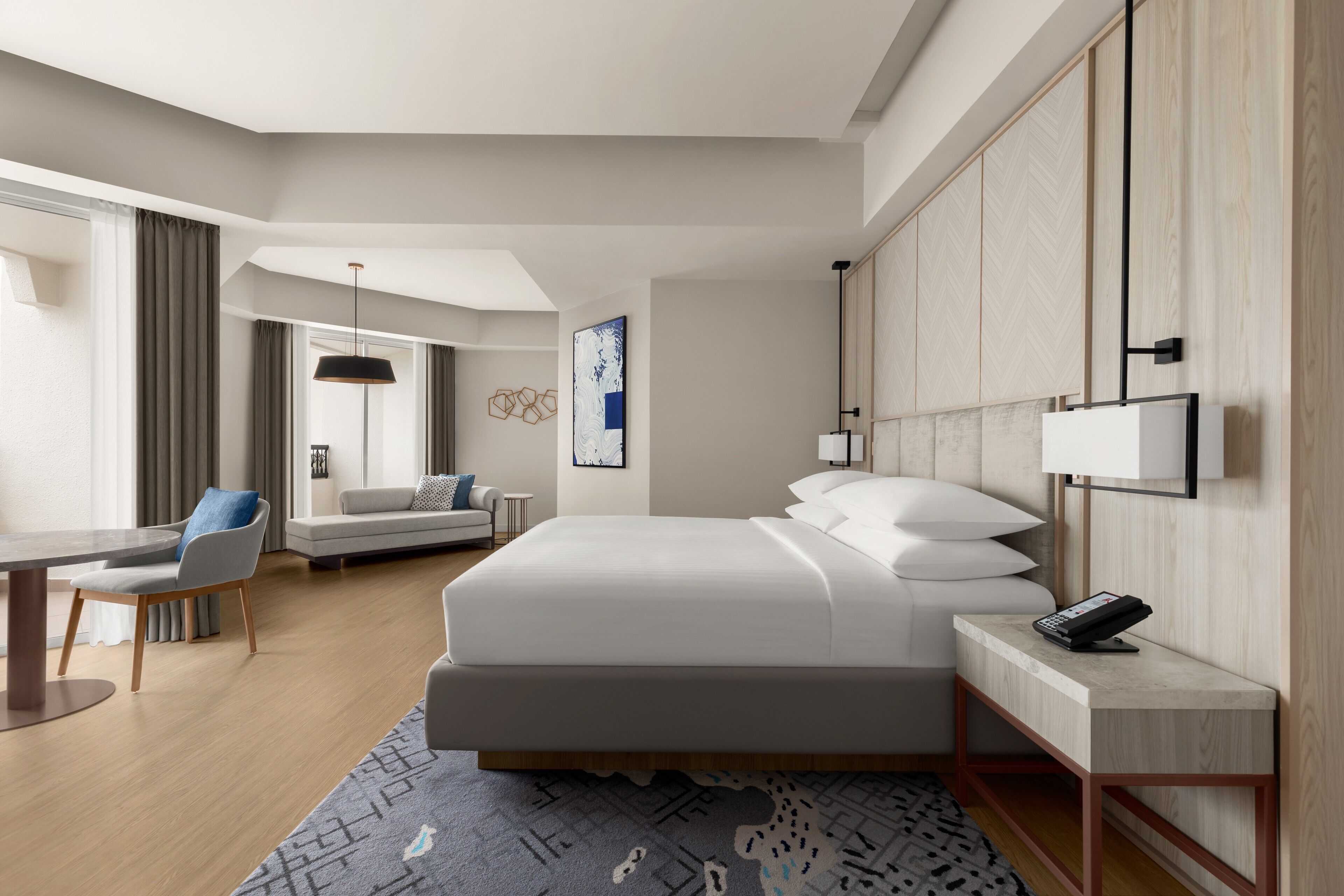 A modern hotel room with a large bed, a desk, a sofa, and a bedside table with a phone.