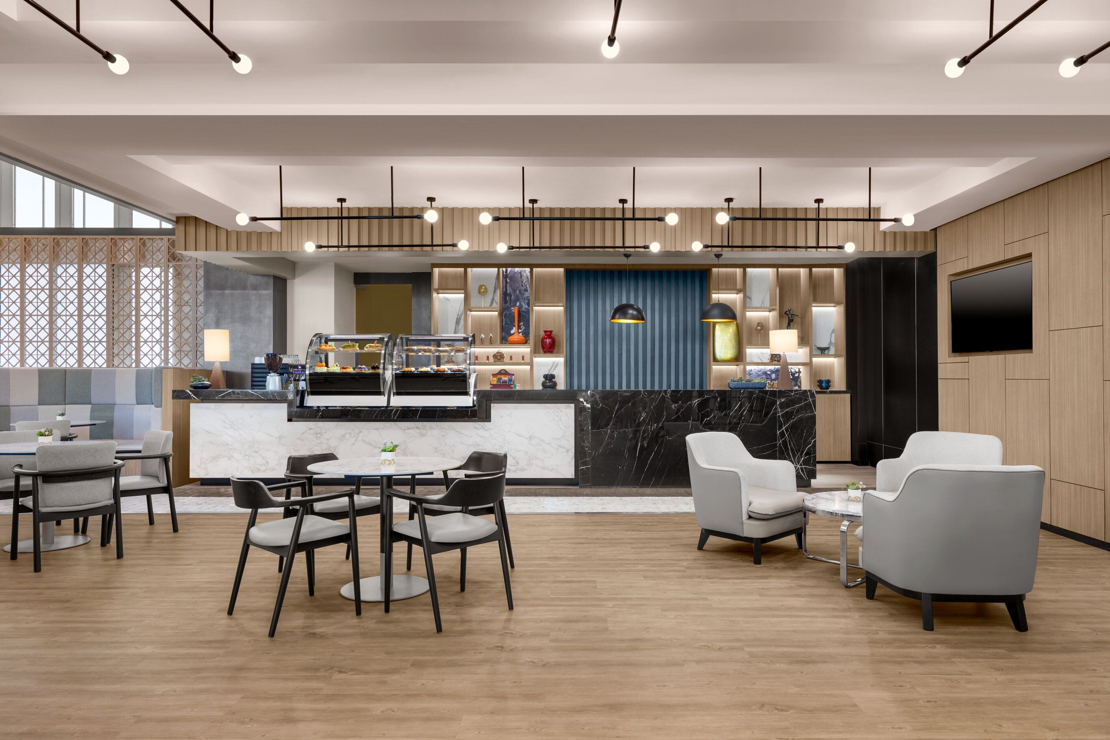 A modern hotel lobby with a marble reception desk, seating area, and a large TV screen.