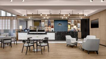 A modern hotel lobby with a marble reception desk, seating area, and a large TV screen.