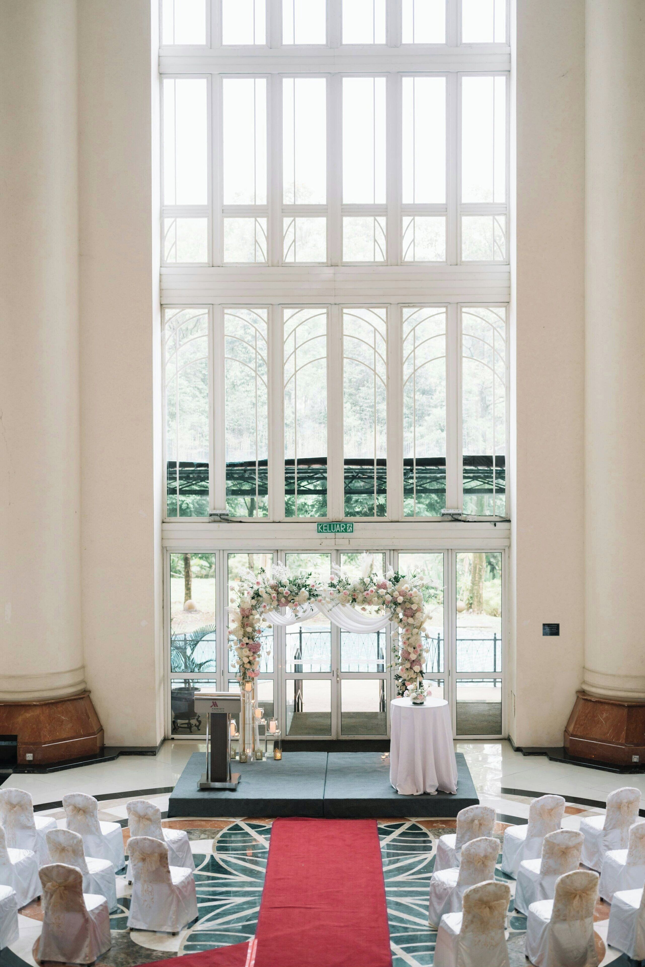 A wedding ceremony setup with a white altar, floral decorations, and a red aisle rug.