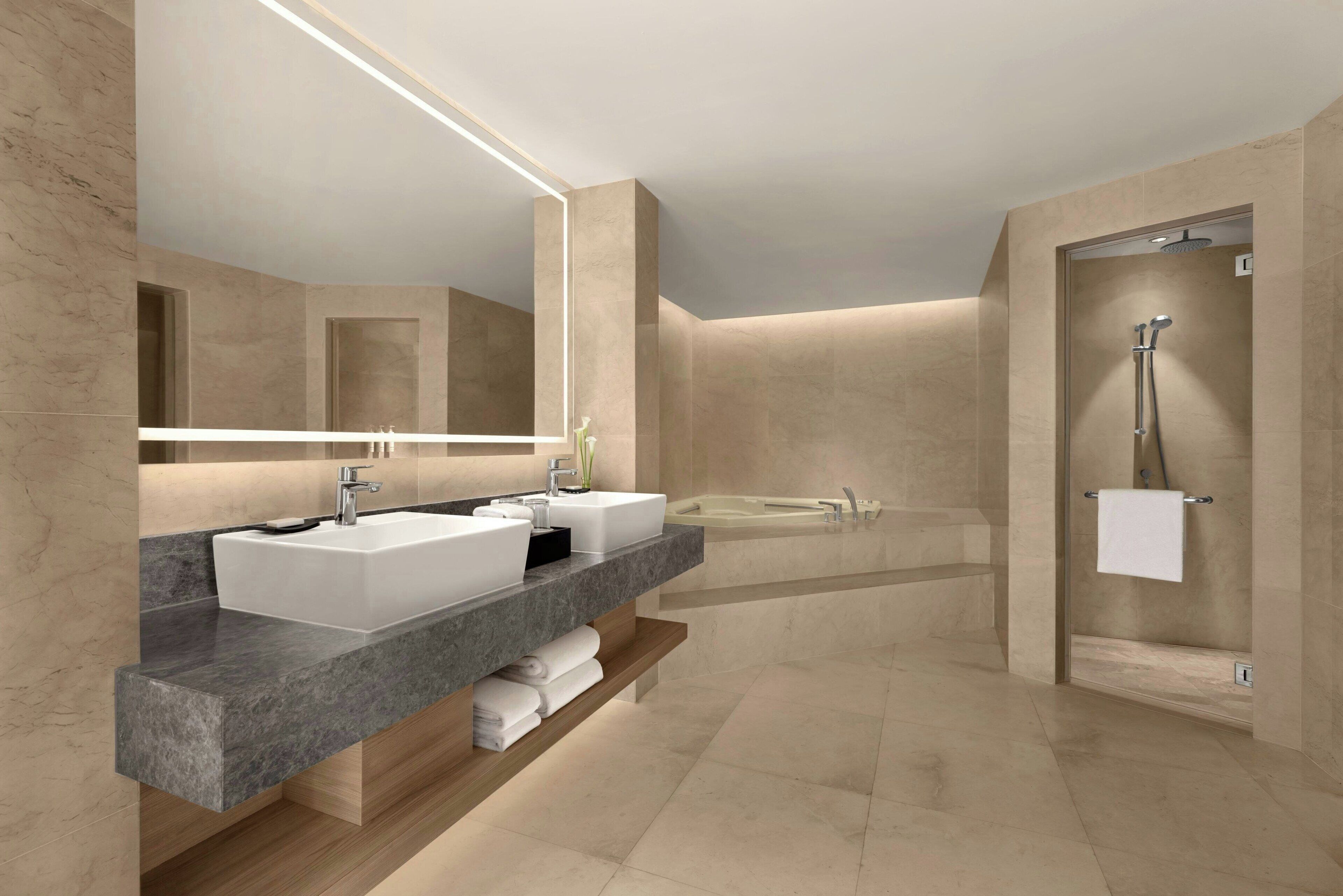 A modern bathroom with a large mirror, two sinks, a bathtub, and a shower.