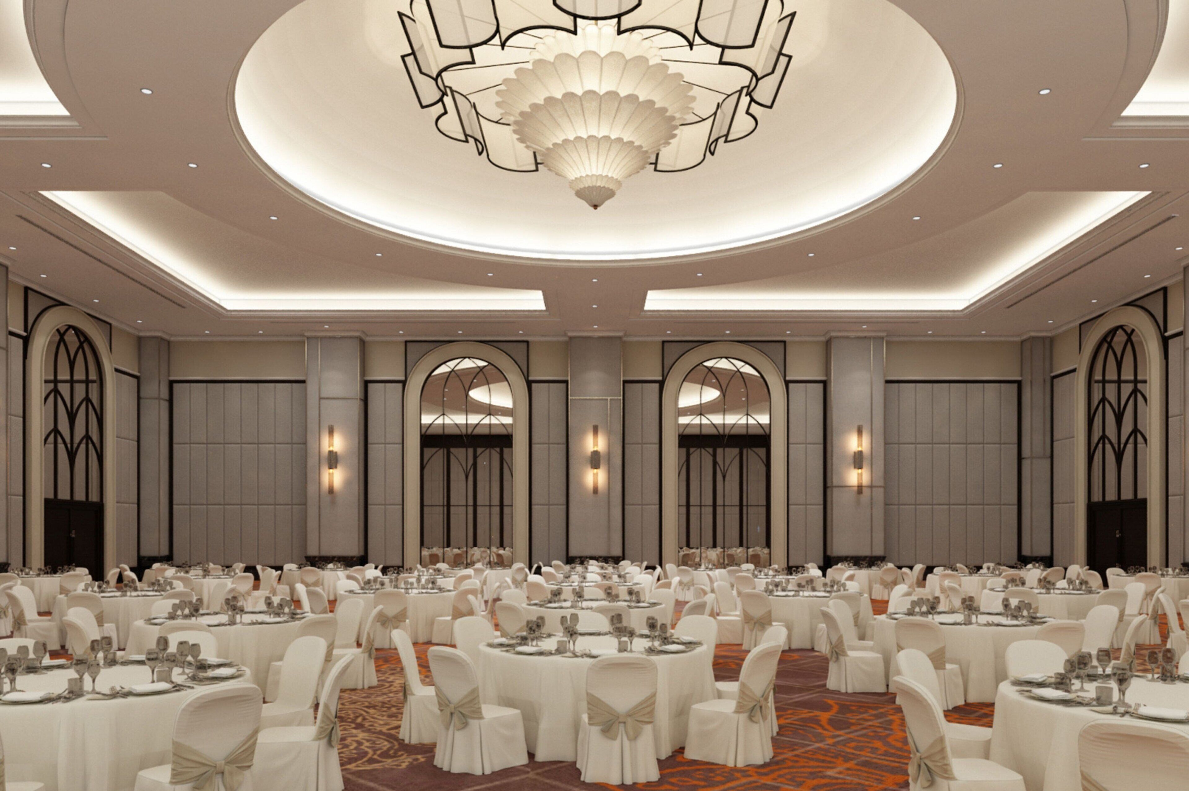 Un amplio salón de banquetes con mesas redondas, sillas blancas y un candelabro central.