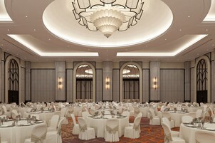 Un amplio salón de banquetes con mesas redondas, sillas blancas y un candelabro central.