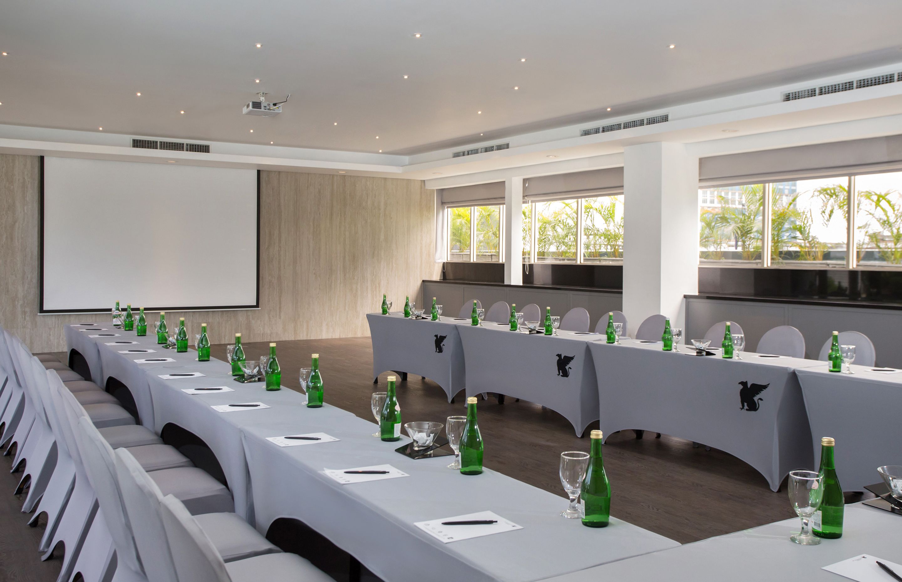 A conference room with a long table set for a meeting, equipped with microphones, nameplates, and green bottles.